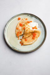 Thin pancakes served with red caviar and cream