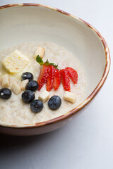 Bowl of oatmeal porridge served with strawberries and blueberries