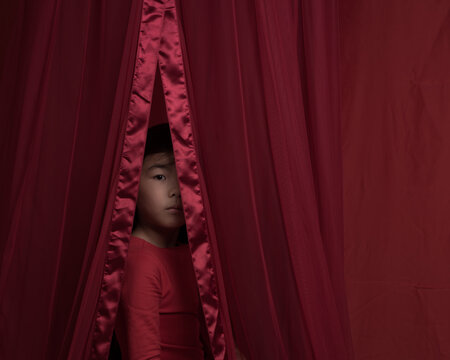 Studio portrait of asian girl in red dress peeking through curtain showing part of her face