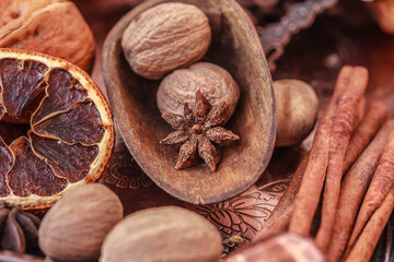 Nutmegs in a wooden scoop, dried orange, Cinnamon sticks, star anise,  on brown metal tray close up.  Spices background