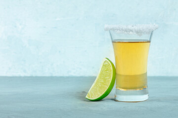 Golden tequila shot with a lime slice, a Mexican drink with a salt rim, side view with copy space
