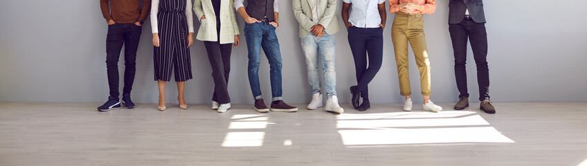 Group of people in modern smart casual clothes posing in fashion studio. Banner with team of business people and company workers standing in row by office wall. Cropped low section shot of human legs