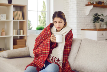 Woman freezes at home. Sick girl wrapped in comfortable blanket is drinking medicine or hot drink...
