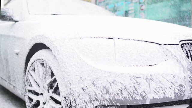 washing a gray bmw car under the pressure of white foam on the street