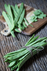 flat green beans tied with string on an old wooden plank in the foreground in focus. wooden plank with cut vegetables in the background. selective focus. copy space, text space. vertical photography.
