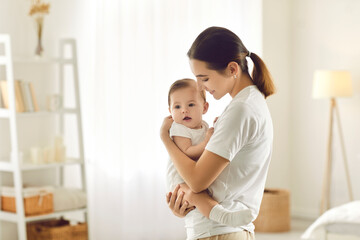 Mother holding baby. Happy beautiful young mom standing in bedroom or nursery room interior in...
