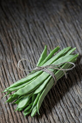 bunch of green flat beans tied with a string on an old wooden plank. sective focus on the front of the image. copy space, text space. background out of focus. vertical photograph.