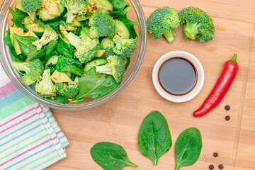 Fresh Green Salad of Avocado, Broccoli, Spinach and Cucumber with Soy Sauce and Red Hot Pepper on Wooden Cutting Board. Vegan Salad. Vegetarian Culture. Raw Food. Healthy Eating and Vegetable Diet