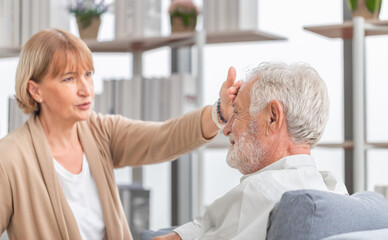 Woman checking fever on forehead by hand, Elderly woman touches the forehead of old husband, Senior...