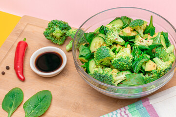 Fresh Green Salad of Avocado, Broccoli, Spinach and Cucumber with Soy Sauce and Red Hot Pepper on Wooden Cutting Board. Vegan Salad. Vegetarian Culture. Raw Food. Healthy Eating and Vegetable Diet