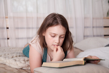 Teenage girl   lying on   bed and reading   book