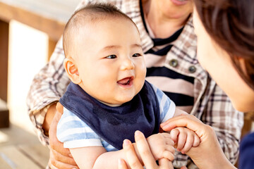 おばあちゃんに抱っこされた赤ちゃんがお母さんと戯れています　3世代が外のベンチに座っています