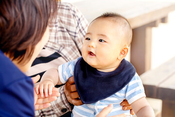 おばあちゃんに抱っこされた赤ちゃんがお母さんと戯れています　3世代が外のベンチに座っています