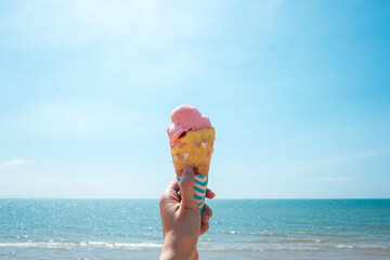Strawberry ice cream in a wafer cone sticking out held in woman`s hand with tropical beach...