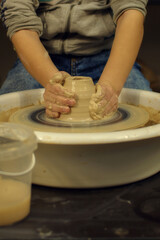 Obraz na płótnie Canvas child potter's hands form by a clay pot on a potter's wheel. The potter works in a workshop