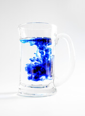glass of water with blue ink dropped in, swirls and twists, in a glass mug isoalted over white, studio photo shot, concept of chemistry or science experiments.