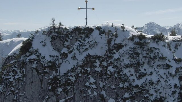Aerial Drone Shot launching upwards showing a rocky mountain wall before finally being up at the peak and the peak cross marking it the highest point of the mountain.