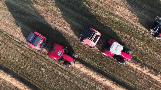Top down aerial shot of some tractors standing ready to start harvesting together with some harvesting machines.