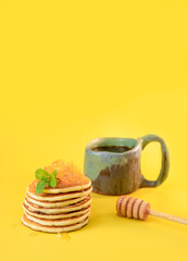 stack of freshly home made pancakes with cup of tea isolated over bright yellow background, traditional americal breakfast meal, studio photo shot. High quality photo