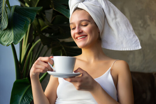 Close-up shot of a beautiful young woman sitting on the balcony with her hair covered with a towel after washing and drinking a coffee.
