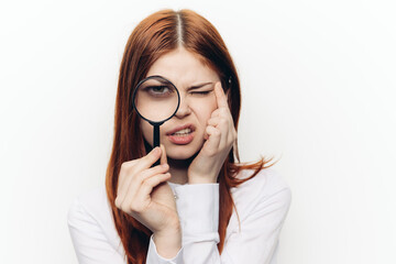 cheerful red-haired woman holding a magnifying glass near her face