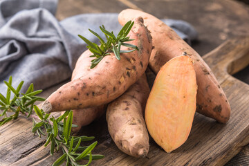 Sweet potato on wooden board background, close up. Raw sweet potatoes or batatas with herbs