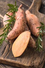 Sweet potato on wooden board background, close up. Raw sweet potatoes or batatas with herbs