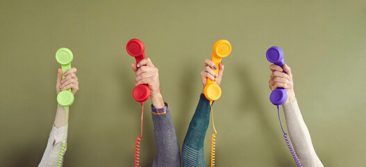 Group of people holding different colourful landline phone receivers. Men and women raising up 4 retro telephone receivers. Banner with four human hands holding phones against green background