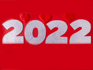 Celebrating the New Year 2022. Shiny numbers 2022 and red hearts on a red background. Flat lay.