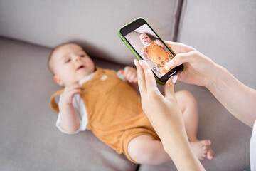 Photo of shiny charming lady wear white t-shirt smiling recording video baby lying sofa inside...