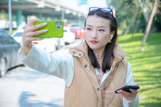 On street sunny day Asian Chinese young woman records video takes pictures has video blog vlog talk show with mobile. Modern way of recording for social media. Phone video call or conference online