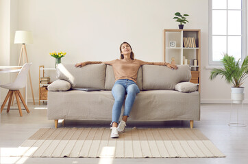 Happy relaxed young woman resting sitting on comfortable sofa in living room at home. Portrait of...