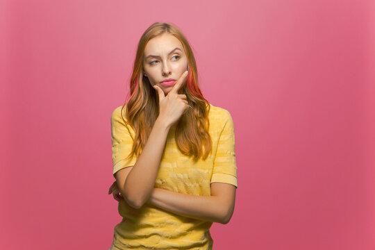 Young girl raised brow rubbing chin scheme plan thinking, pondering answer on pink studio background with copyspace