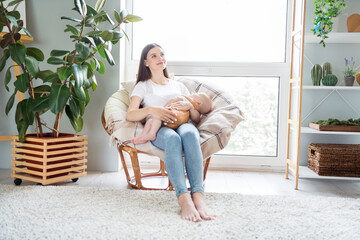 Obraz premium Photo of dreamy inspired mother sit armchair barefoot hug infant child sleep wear white t-shirt home indoors