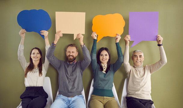 Group of happy people holding up clean, colorful mock up paper banners. Four smiling males and females sitting in row and showing blue, orange and purple speech balloons and message bubbles