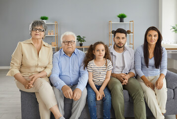 Family watching television sitting on couch at home. Front view of multigenerational Caucasian family sitting together on sofa and watching modern interesting TV show. People and entertainment concept