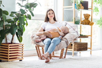 Photo of shiny dreamy mother dressed white t-shirt sitting chair holding hands arms sleeping child inside indoors apartment room