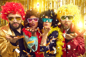 Happy merry diverse people dressed in boas, glasses and curly Afro wigs celebrating New Year at...