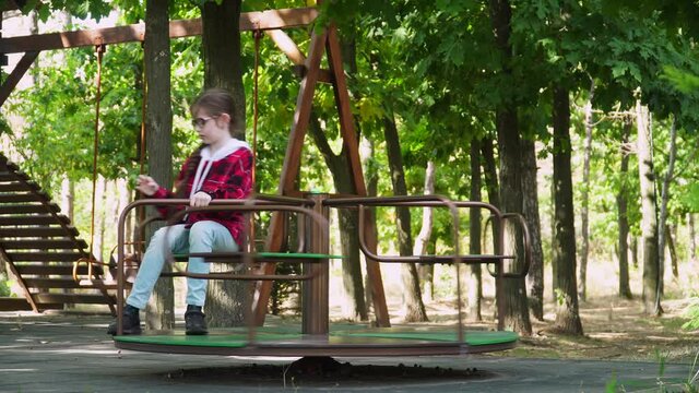 girl rides on swing waving her hand. Cute baby girl enjoying swing in the park