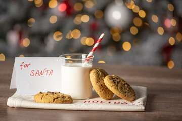 christmas cookies with a glass of milk and a letter for santa on background of blurred lights