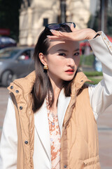 Beautiful stunning Asian business woman walks around streets of Chinese metropolis city during sunny fall day. Long hair, wears glasses covers face from sunlight. Looking at camera portrait.