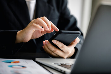 Close up of Businesswomen or Accountant using a smartphone and laptop computer with analyzing business report graph and finance chart at the workplace, financial and investment concept.