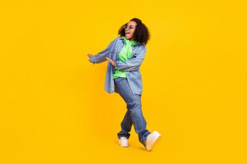 Fototapeta na wymiar Photo of pretty attractive afro woman wear denim jacket dark glasses smiling dancing isolated yellow color background