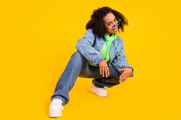 Photo of charming funny african lady dressed jeans green hoodie dark eyewear sitting smiling isolated yellow color background