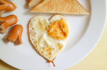 Delectable breakfast dish of heart shaped fried egg, sausages and toasts
