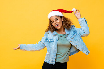 Portrait of joyful African American woman wearing Christmas hat with open palm gesture on yellow isolated background