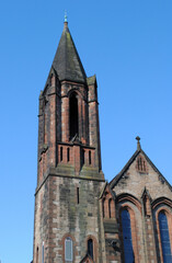 Fototapeta na wymiar Old Stone Church with Tower & Spire seen against Blue Sky