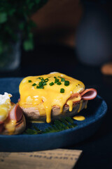 egg Benedict with hollandaise sauce on dark blue plate on table in kitchen