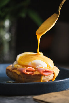 egg Benedict with hollandaise sauce on dark blue plate on table in kitchen