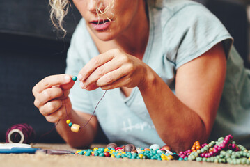 Close up of young adult woman busy in jewelry cheap wooden beads making of bracelets and necklace....